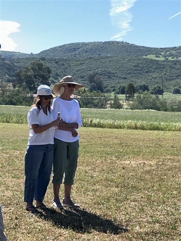 Two people standing in a grassy field with hills in the background.
