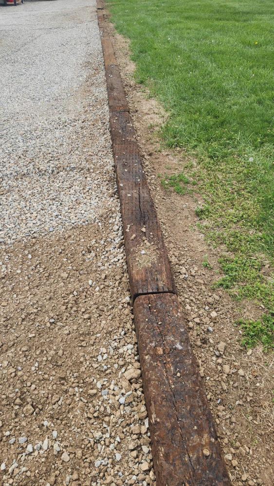 Gravel path bordered by wooden beams, grassy field to the right.