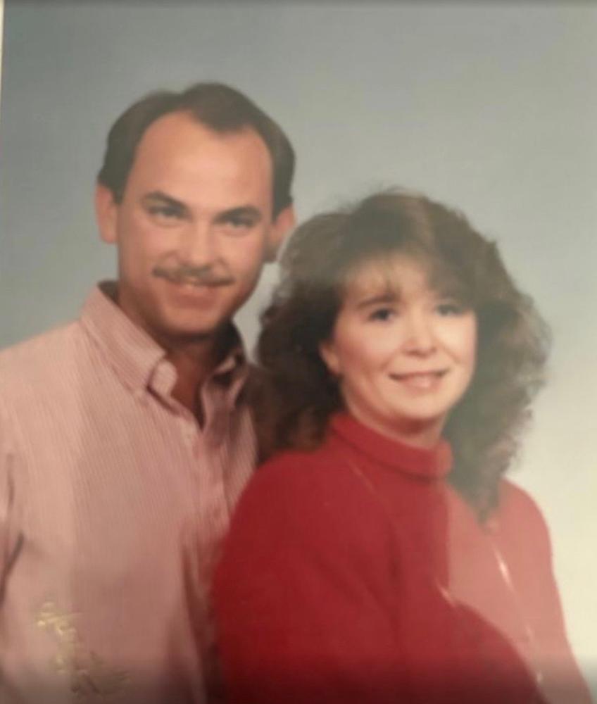 A man and woman smiling, standing close, against a light gray background.