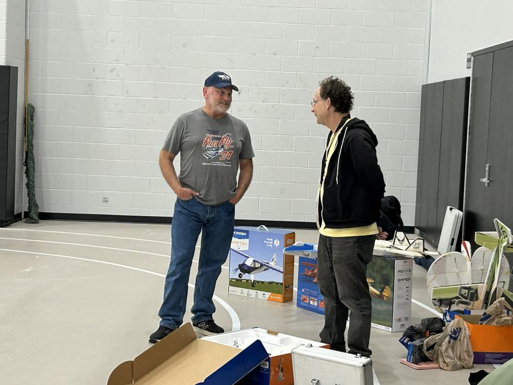 Two men stand talking in a room with boxes and model planes.