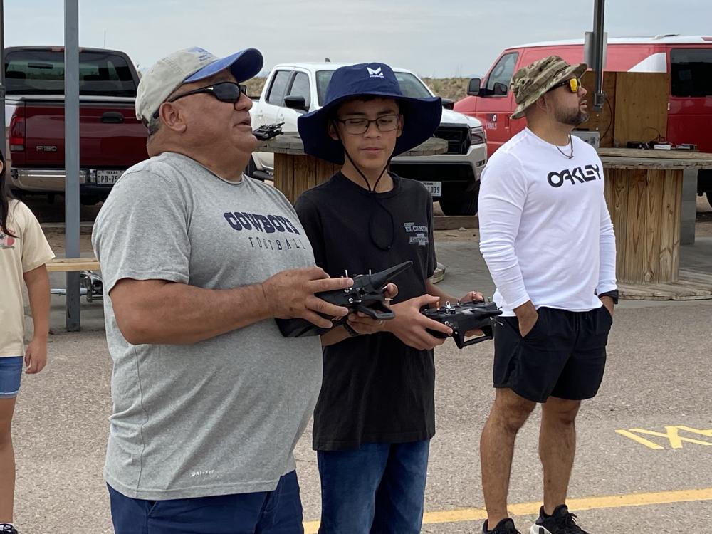 Two people outdoors operating drones with controllers.