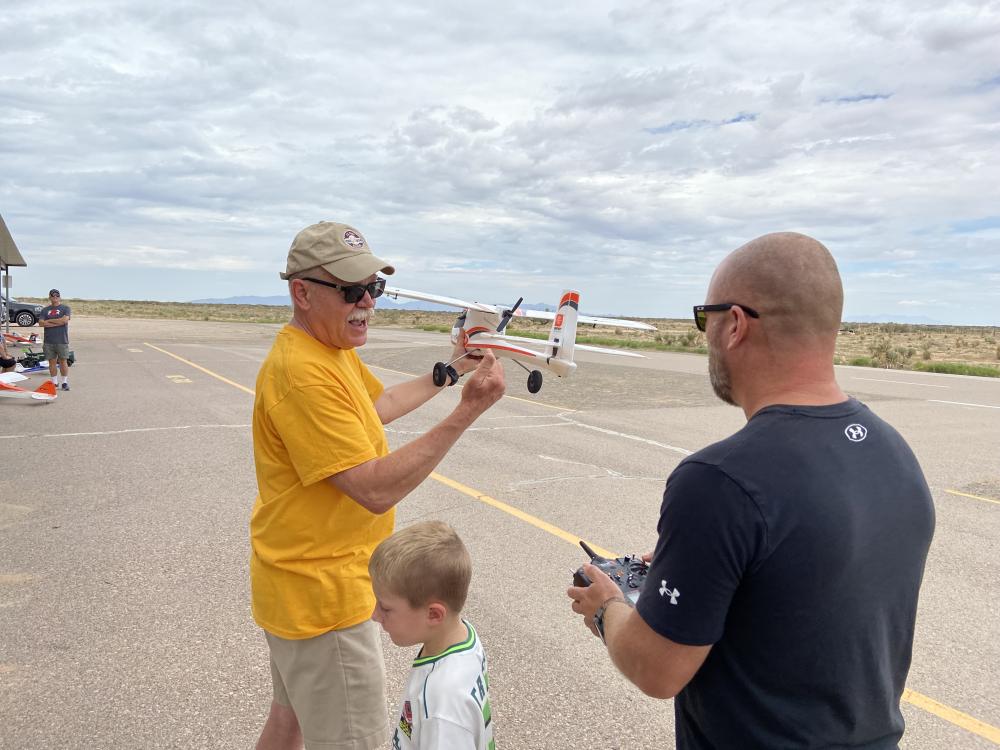 Two men with model airplane, boy watching, wide open sky.