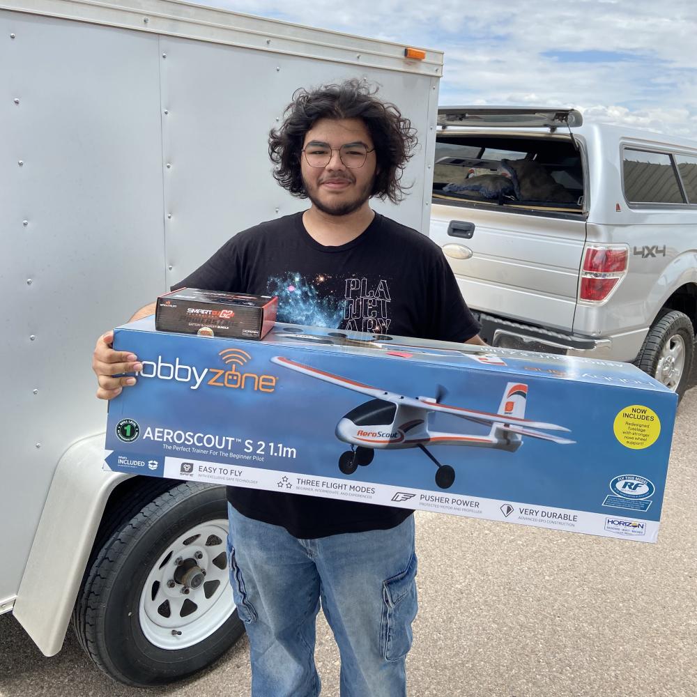 Man holding a large airplane model box and a small box, standing by a trailer.