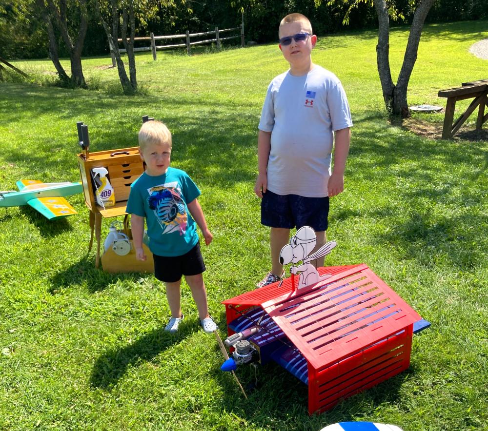 Two children stand on grass with colorful Snoopy-themed doghouse planes.