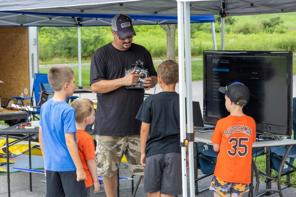 Man showing remote control to four kids under a canopy.