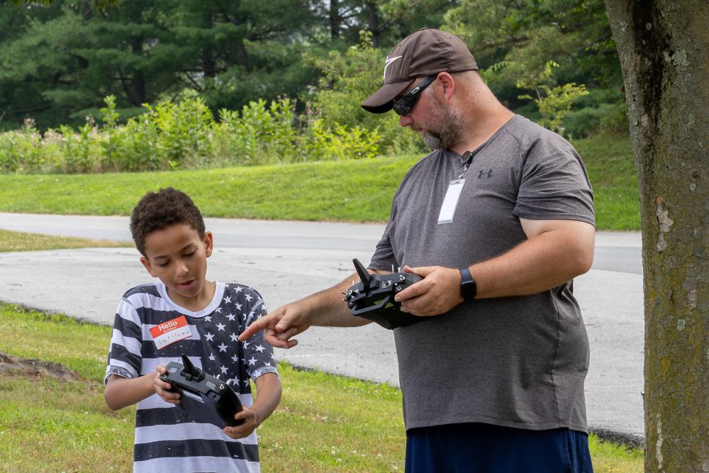 Boy and man operate remote controls outdoors, focused on tasks.