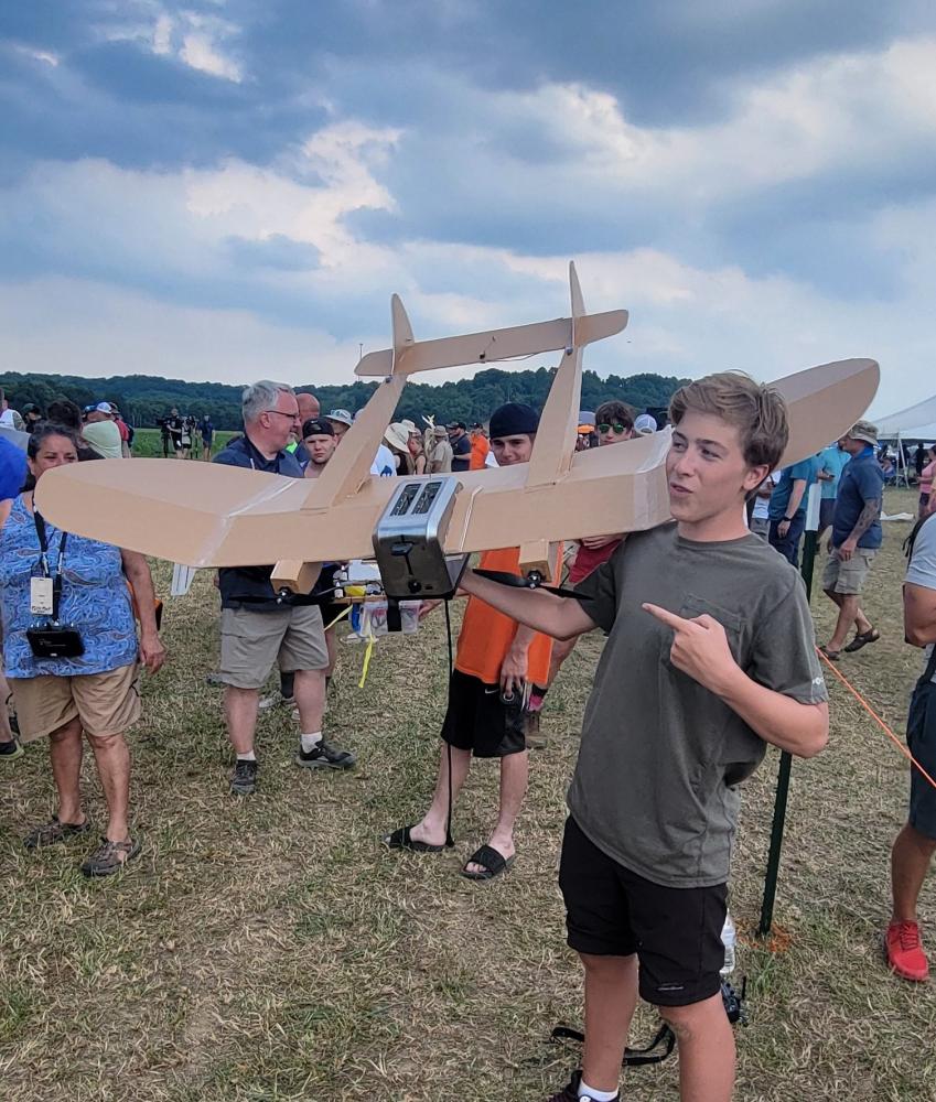 Boy with model aircraft at outdoor event, cloudy sky in background.