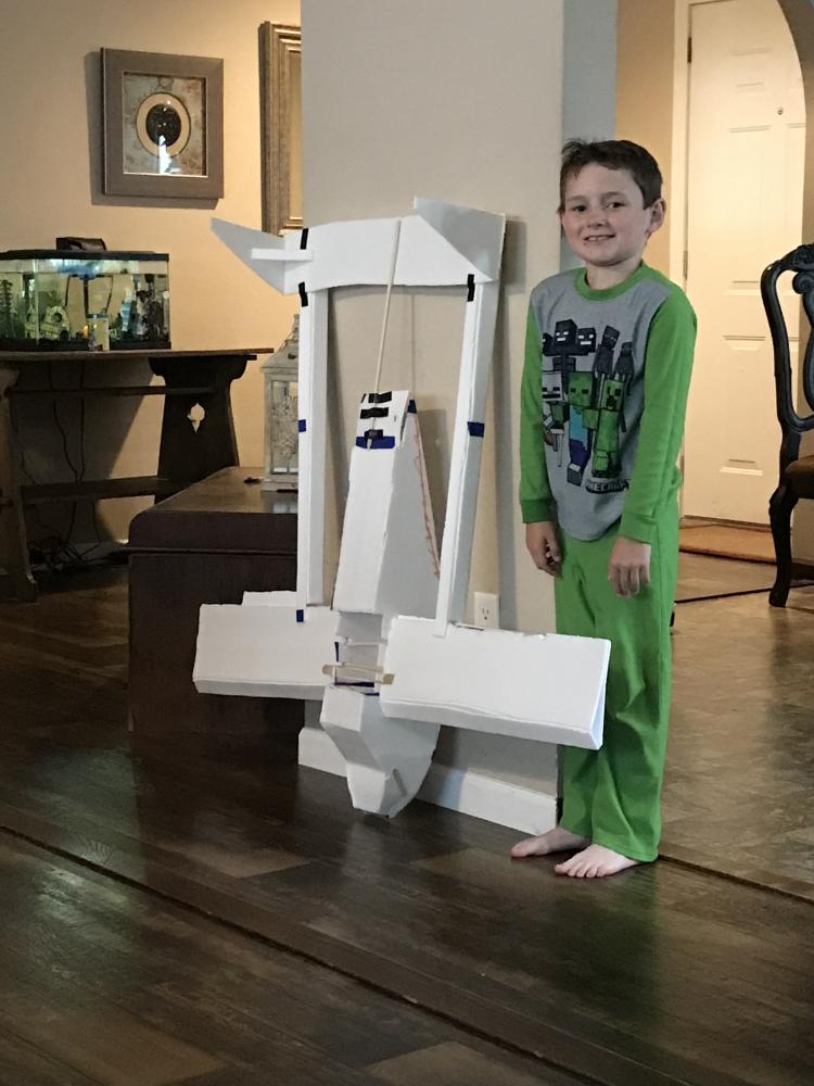 Child smiling beside a large foam model in a living room setting.
