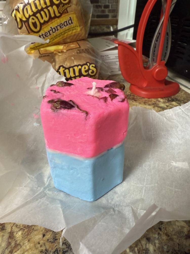 Pink and blue square candle with dried flowers on top.