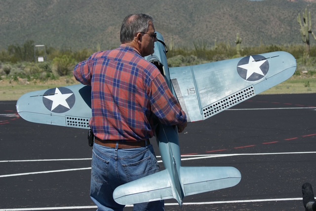 A man holding a large model plane with military markings, standing on a tarmac.