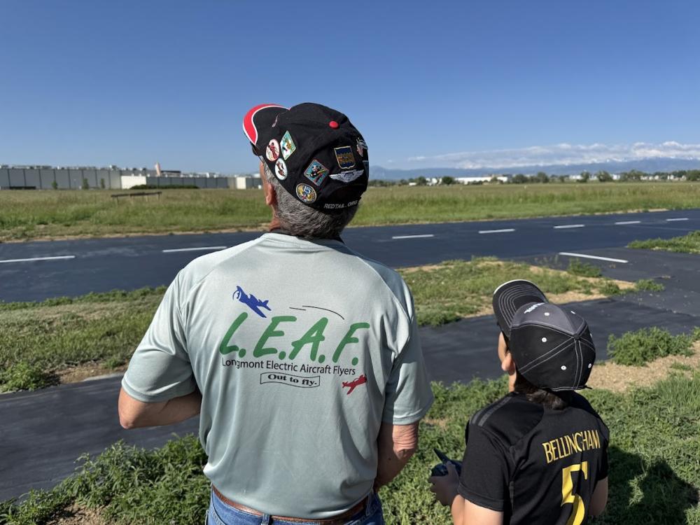 Two people watching model planes at an outdoor field.