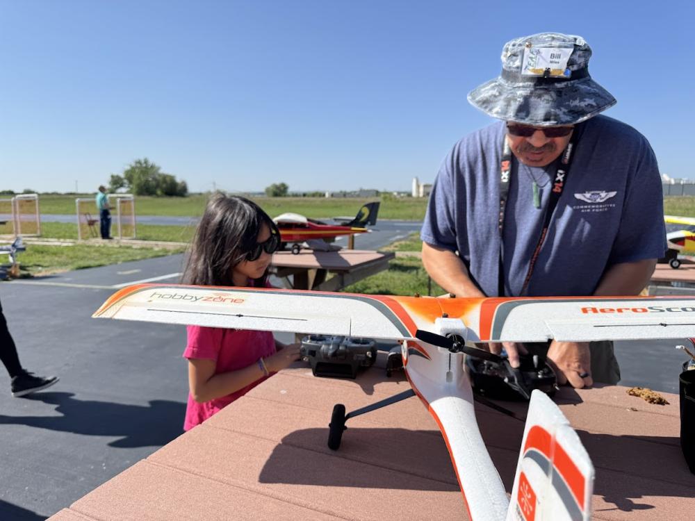 Man and child with model plane on outdoor table, sunny day.