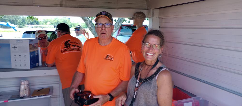 Two people smiling, wearing bright orange shirts indoors at an event.
