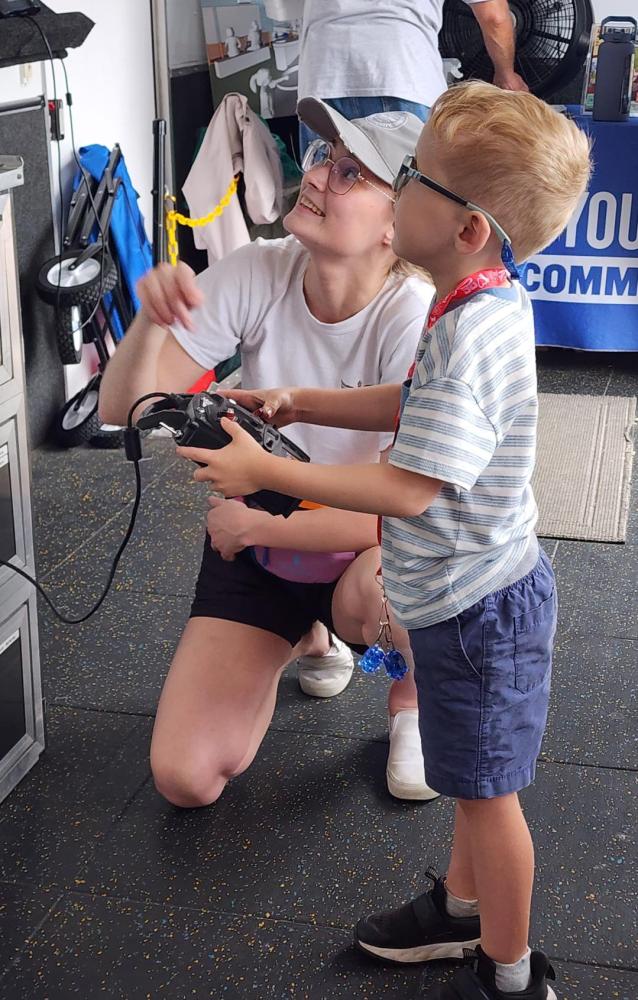 A woman and boy engaging with a device, both wearing sunglasses indoors.