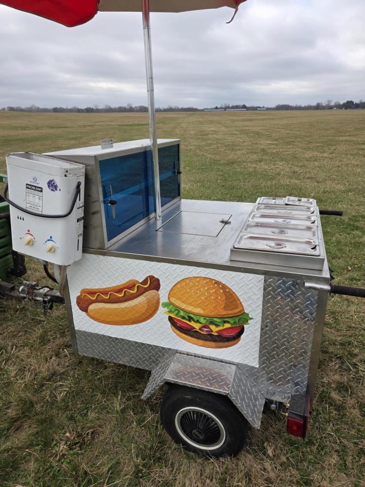 Food cart with hot dog and hamburger illustrations in an open field.