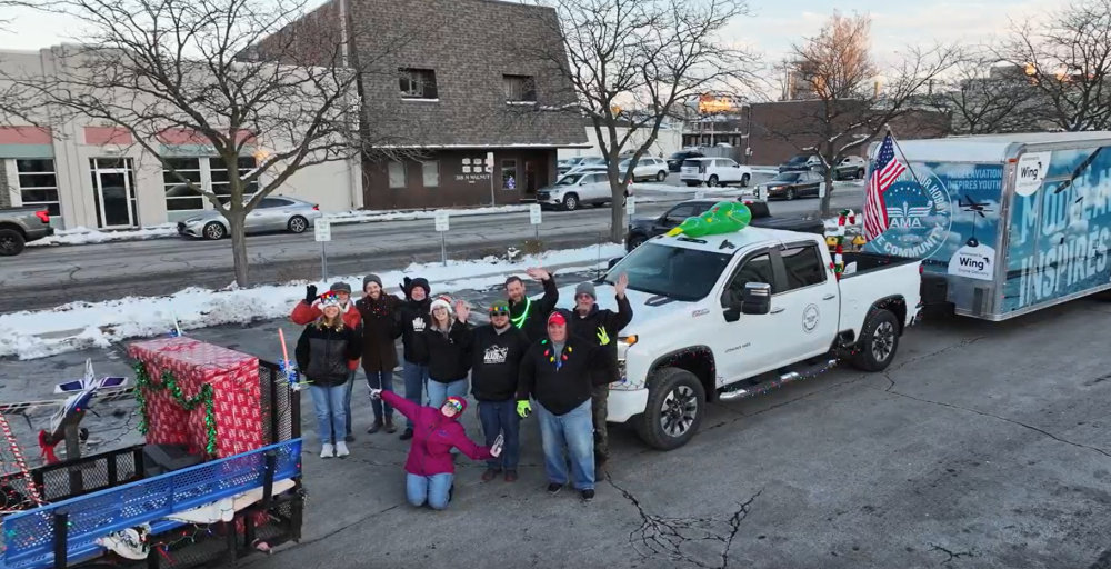 Group posing near truck with decorated trailer, snowy street setting.