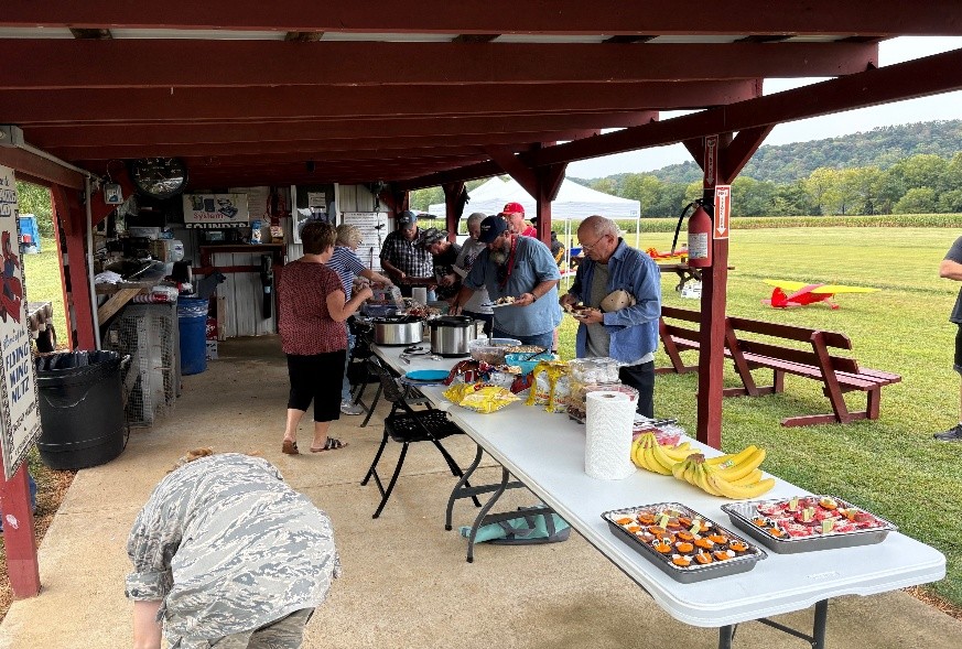 People enjoying a picnic buffet under a pavilion, surrounded by greenery.