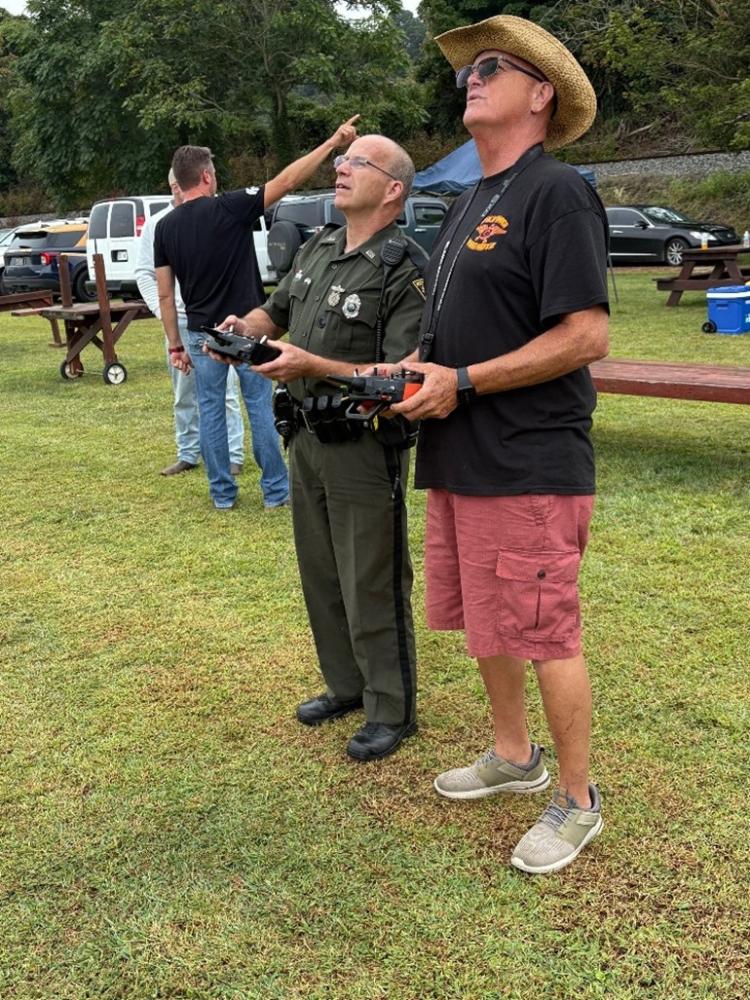 Two men focused, holding remote controls in a grassy park setting.