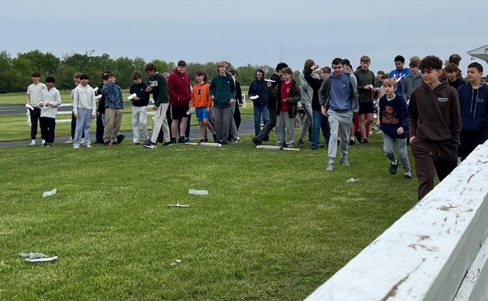 A group of people walking on a grassy field near a white fence.
