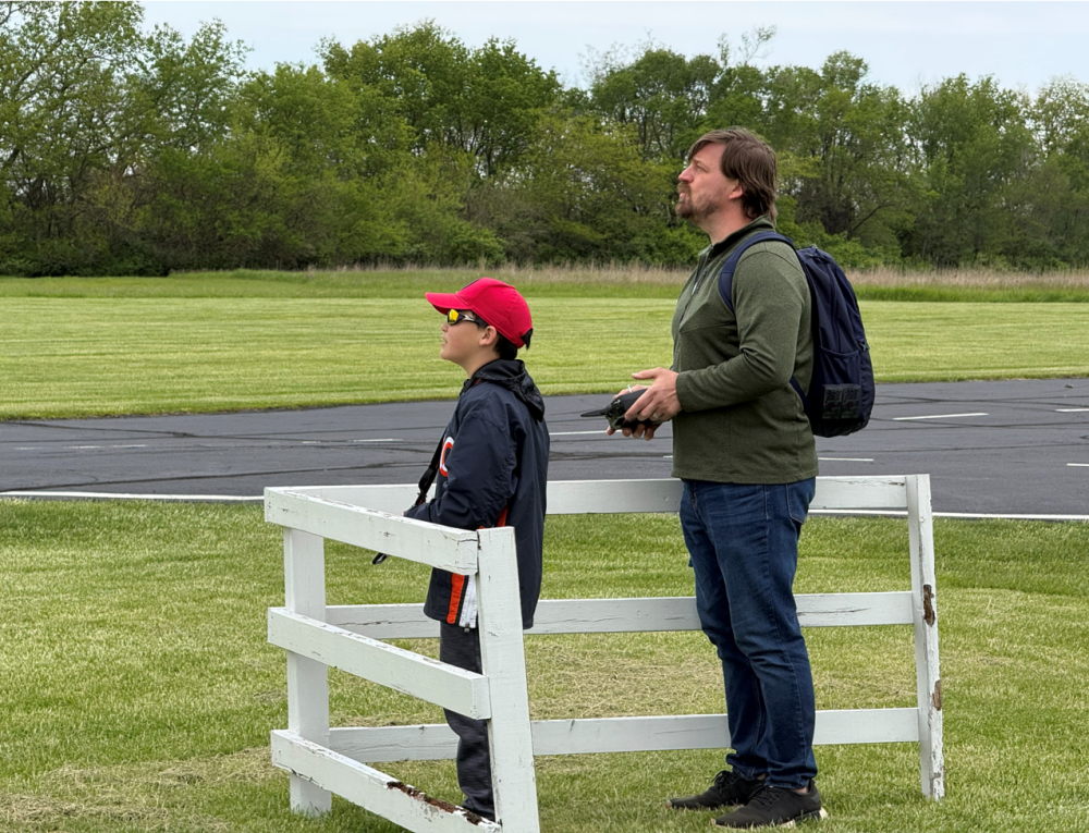 Man and boy standing by a white fence, watching something intently.