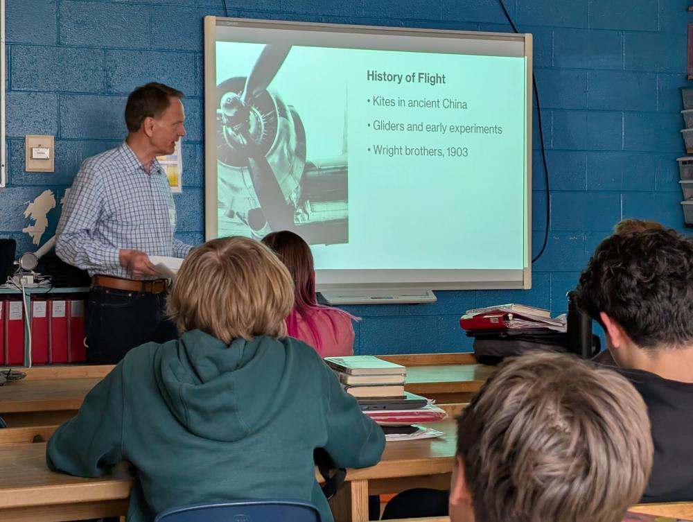 Teacher in classroom presenting a slide about flight to students.
