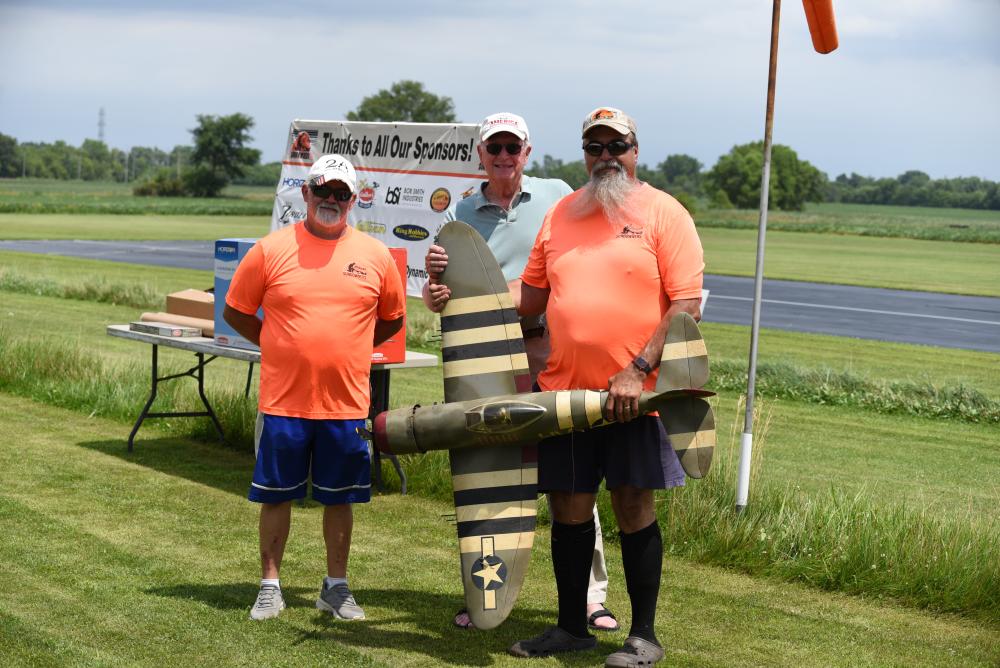 Three men outdoors, holding a model military aircraft.