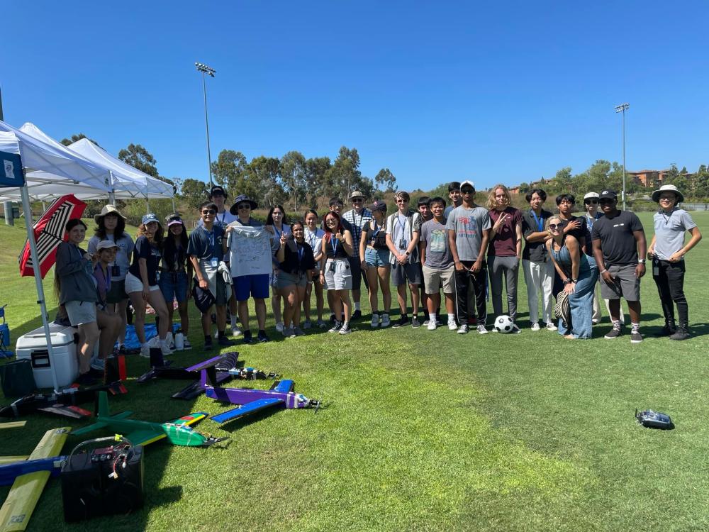 A group of people standing on a sunny field beside tents and colorful model planes.