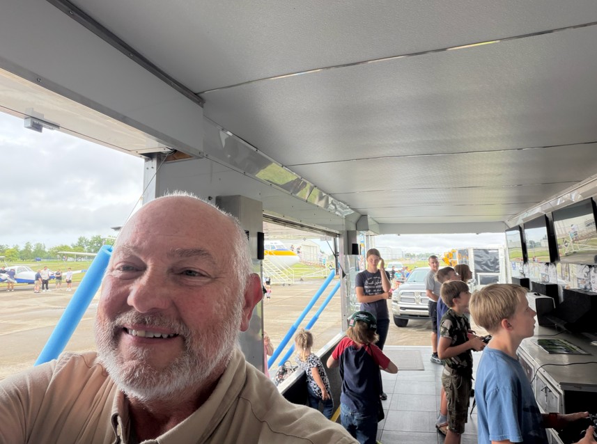Man smiling indoors with children playing arcade games.