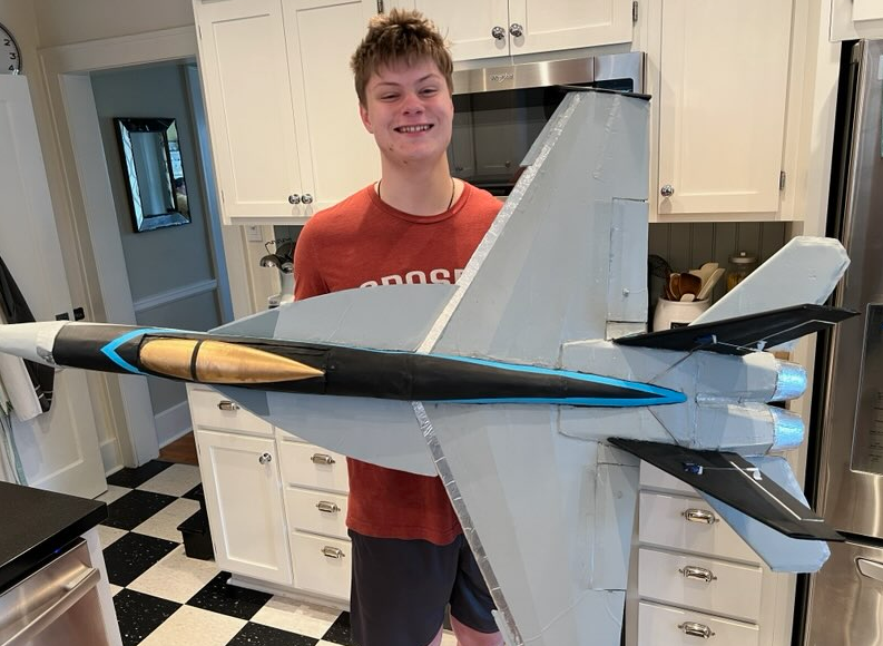Boy smiling, holding large model jet in a kitchen.