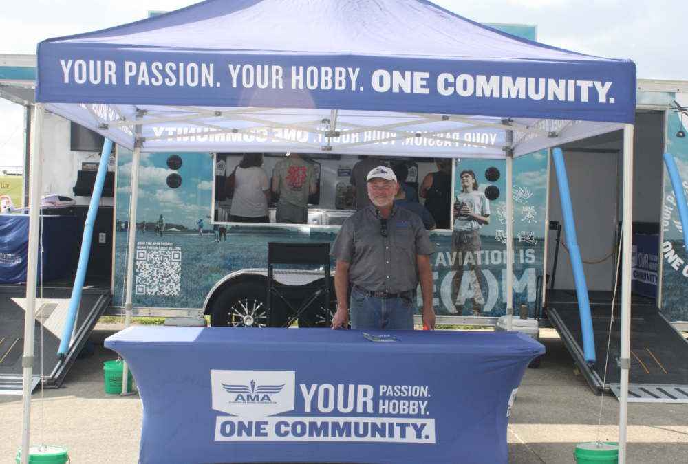 Booth with smiling man under a blue tent at an outdoor event.