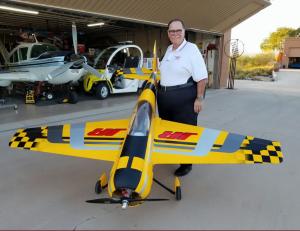 Man smiling beside a large yellow and black model airplane in hangar.