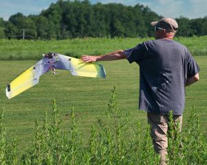 Man launching a small yellow drone in a grassy field.