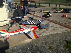 Model airplanes on a paved area, person crouching nearby, sunny day.