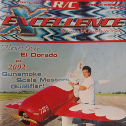 Man smiling next to a red model airplane on a runway, under a blue sky.
