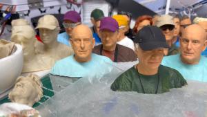 3D printed models of men wearing caps, in various colors, displayed on a shelf.