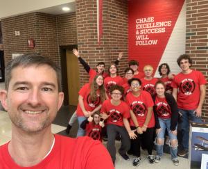 Group of people in matching red shirts smiling in a school hallway.