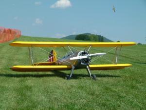 Yellow biplane on grass runway with hills in the background.