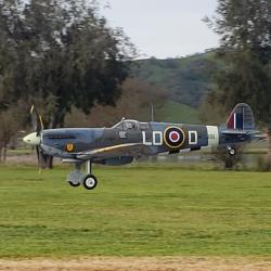 Vintage fighter plane flying low over grassy field.