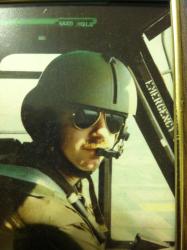Pilot in a helmet and sunglasses inside a cockpit.