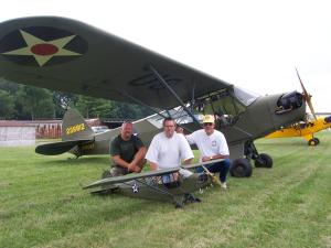 People kneeling on grass with model and full-size vintage military planes.
