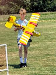 Teen holding a yellow model airplane on a grassy field.