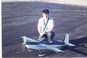 Man kneeling beside a large model airplane on a paved surface.