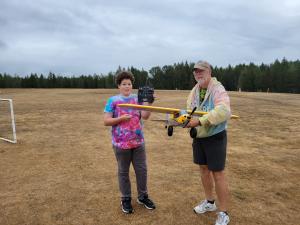 Man and boy with model airplane on grassy field.