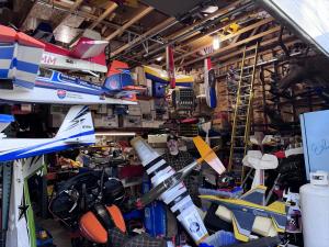 Crowded garage with model planes and a man holding a model aircraft.