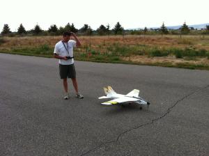 Remote-controlled jet on runway, person holding controller nearby.