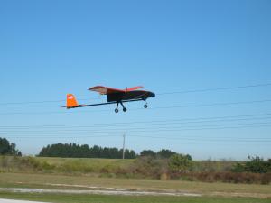 Drone with orange wings flying over grassy field.