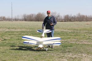 Man with red cap and blue jacket standing outdoors with a large model biplane.