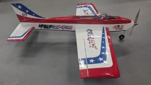 Aerobatic model plane with red, white, and blue design on gray floor.