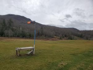 Wind sock on pole near bench in grassy field, mountains in the background.