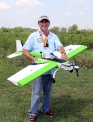 Man holding a large model airplane outdoors on a grassy field.